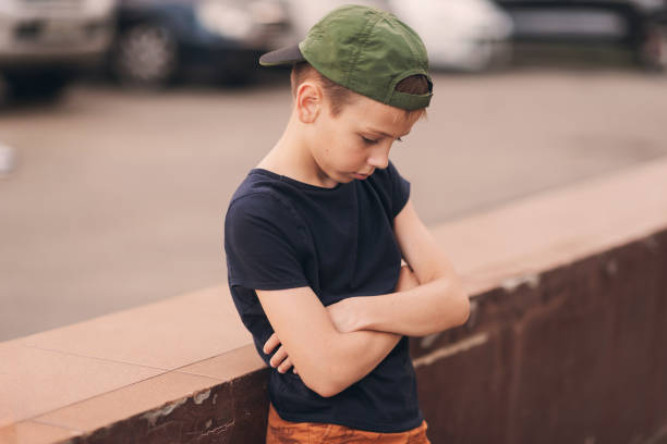 A teenage boy is squatting leaning against a concrete wall on the street. Upset and sad. Bullying. Quarrel with parents A teenage boy is squatting leaning against a concrete wall on the street. Upset and sad. Bullying. Quarrel with parents. sad teenager boy crying outdoors in park stock pictures, royalty-free photos & images