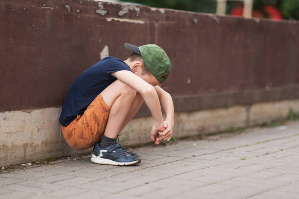 A teenage boy is squatting leaning against a concrete wall on the street. Upset and sad. Bullying. Quarrel with parents A teenage boy is squatting leaning against a concrete wall on the street. Upset and sad. Bullying. Quarrel with parents. sad teenager boy crying outdoors in park stock pictures, royalty-free photos & images