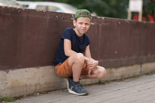A teenage boy is squatting leaning against a concrete wall on the street. Upset and sad. Bullying. Quarrel with parents A teenage boy is squatting leaning against a concrete wall on the street. Upset and sad. Bullying. Quarrel with parents. sad teenager boy crying outdoors in park stock pictures, royalty-free photos & images