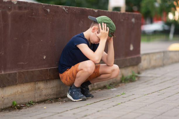 A teenage boy is squatting leaning against a concrete wall on the street. Upset and sad. Bullying. Quarrel with parents A teenage boy is squatting leaning against a concrete wall on the street. Upset and sad. Bullying. Quarrel with parents. sad teenager boy crying outdoors in park stock pictures, royalty-free photos & images