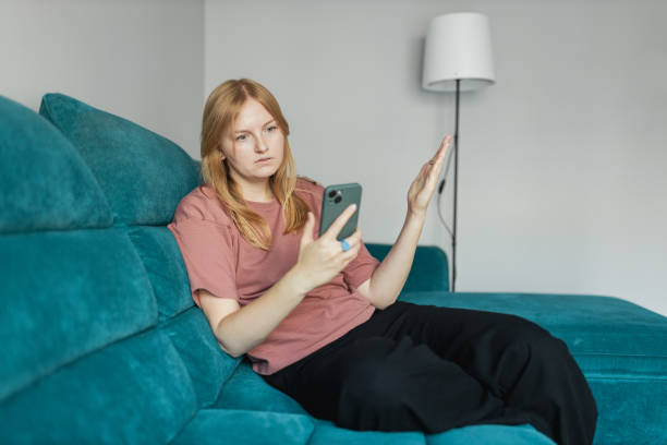 istock Upset sad, skeptical, serious woman holding smartphone gadget for communicate indoors. Negative people emotion, pensive girl sitting on sofa at home. 30s woman holding smartphone. 2200447680