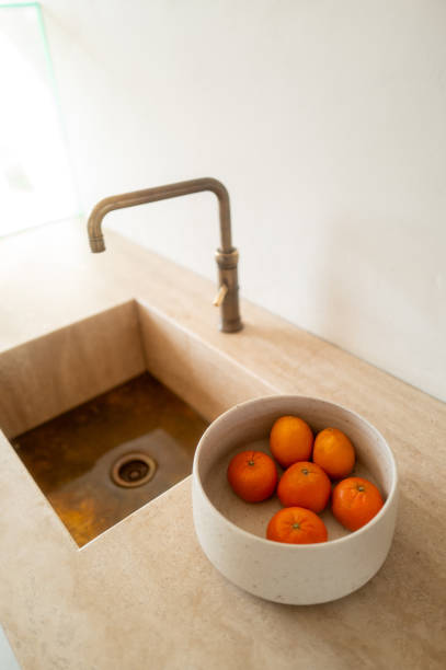 Minimalist kitchen features a bowl of tangerines next to a modern sink, showcasing simple elegance and natural elements