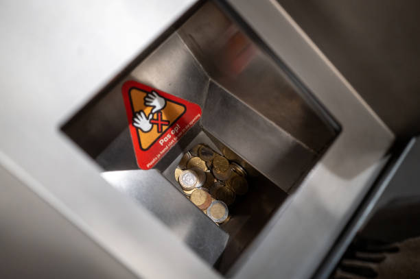 Euro coins falling into a self-checkout machine deposit slot with a warning sign in dutch