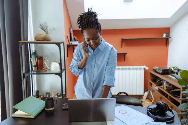 istock Young woman working remotely using laptop and phone in a modern setting 2200449777