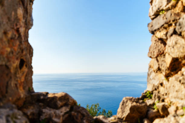 A tranquil view of the serene ocean seen framed through ancient stone ruins under a clear sky, evoking a sense of peace, nature, and historical timelessness.