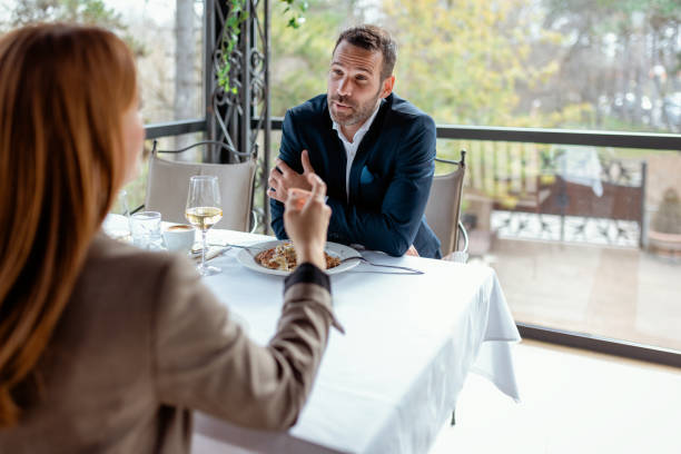 Two Professionals, a Man and a Woman, Having a Focused Discussion Over Lunch in a Stylish Café. They Are Exchanging Ideas, While Enjoying Their Meals. The Natural Light and Casual Setting Emphasize a Balance Between Work and Leisure. Ideal for Content About Teamwork, Entrepreneurship, or Professional Development