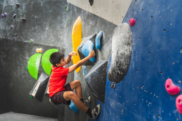 Child climbing a bouldering wall, trying hard to reach at top, practicing and learning new skills in the bouldering gym.