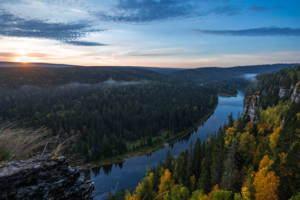 istock As the sun rises, golden light spills across a winding river, casting shadows on towering cliffs and vibrant autumn trees. Mist lingers above the water, enhancing the serene beauty of the forest 2200464367