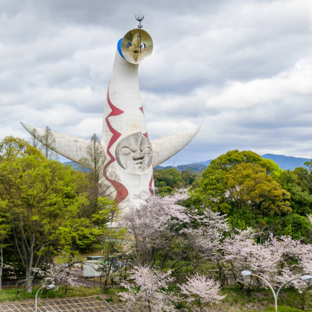 Osaka, Japan - April 9, 2024: The iconic Tower of the Sun, built for Osakas 1970 World Expo, stands tall amidst blooming cherry blossoms. A symbol of technological optimism, it's now a park landmark.