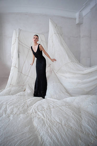 istock model wearing a black gown elegantly poses in a minimalist studio setting. backdrop consists of large abstract white fabric shapes, creating a striking contrast 2200464769