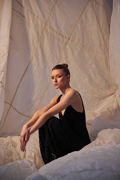 istock Model sits gracefully on a white fabric backdrop in a minimalist studio. She wears a black outfit that contrasts with the soft textures around her, capturing a moment of serene beauty 2200464772