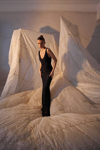 istock Striking model stands gracefully in a form-fitting black gown, surrounded by elaborate folds of light-colored fabric that create a unique artistic ambiance within the space 2200464776