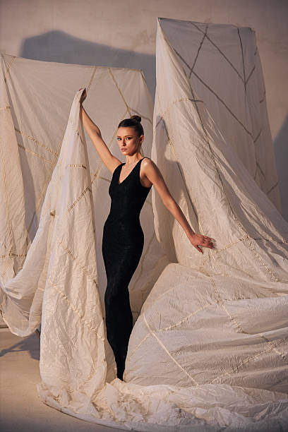 istock Fashion model showcases elegance while holding draped fabric in a minimalist studio. The light and shadows create a captivating atmosphere that highlights the design 2200464782