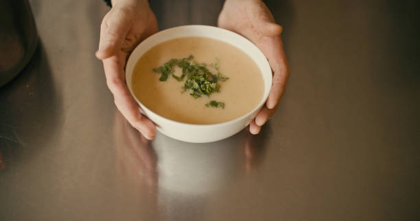 Close-up view of a hand holding a bowl of roasted swede and parsnip soup for a vegan diet