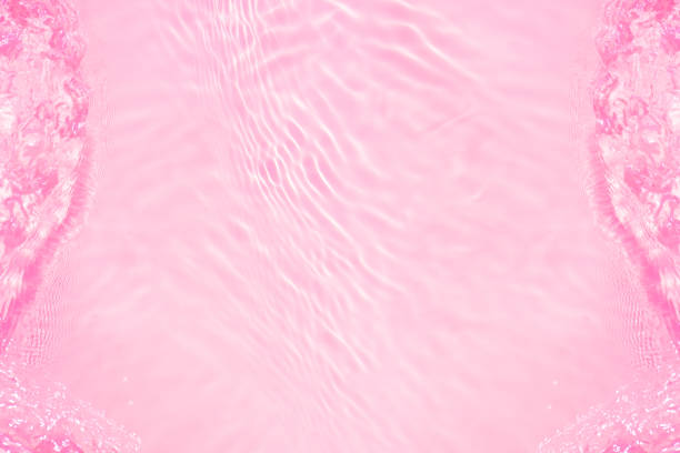 Pink water bubbles on the surface ripples. Defocus blurred transparent pink colored clear calm water surface texture with splash and bubbles. Water waves with shining pattern texture background
