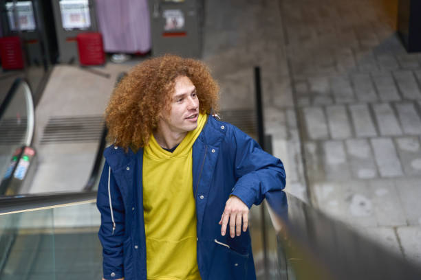istock Young man with curly hair using escalator in urban setting 2200475251
