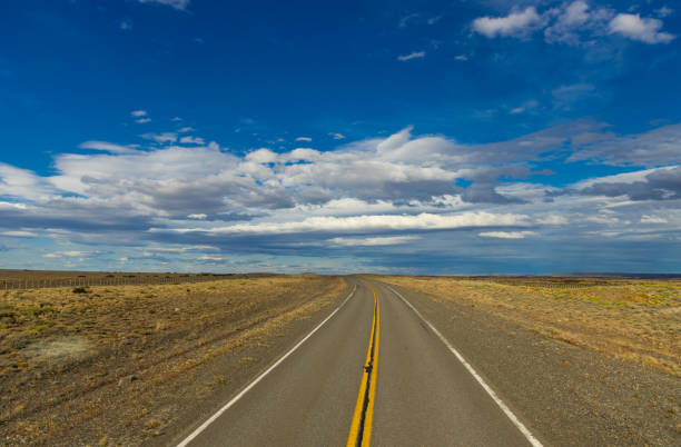 istock A long, empty road stretches endlessly through a vast, arid landscape under a bright blue sky with scattered clouds 2200476230