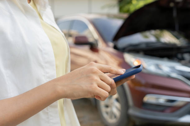 istock breakdown, broken car, repair. Woman uses mobile phone check insurance premiums through application due to car accident . Find garage to get car fixed during country tour, waiting for help, emergency. 2200481053