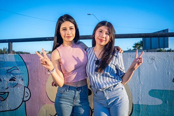 istock Two women are standing side by side, both giving a cheerful peace sign 2200498654