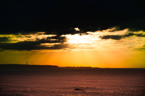 A stunning sunset over Tamsui with wind turbines silhouetted against a dramatic sky. The sky is filled with rich light and shadow variations, creating a captivating scene. Tamsui, Taiwan.