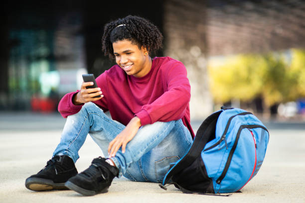 istock Man using smart phone while sitting outdoors with backpack on city street 2200506039