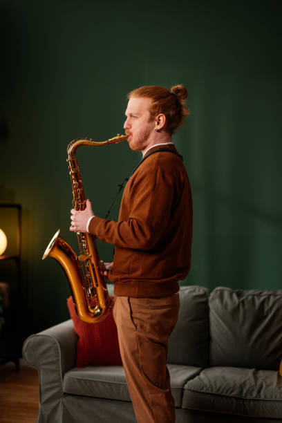 Young musician with vibrant red hair and a beard, passionately playing the saxophone in a cozy living room setting