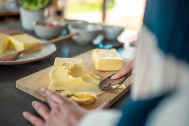 Close up on hands of a mid adult mixed race woman skillfully creating a butter board in her modern kitchen. Focus on her hands spreading butter with a wooden knife, surrounded by fresh ingredients.