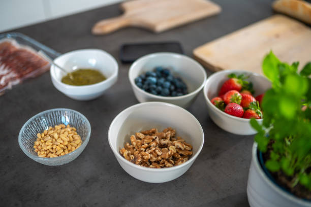 A selection of butter board ingredients on a kitchen counter, including walnuts, blueberries, strawberries, pine nuts, and pesto. Perfect for crafting a flavorful and artistic culinary spread.