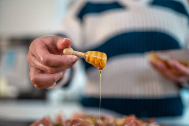 Lovely mid adult mixed race woman adds honey to a butter board in her home kitchen. She wears a cozy striped sweater, creating a warm, inviting culinary atmosphere.