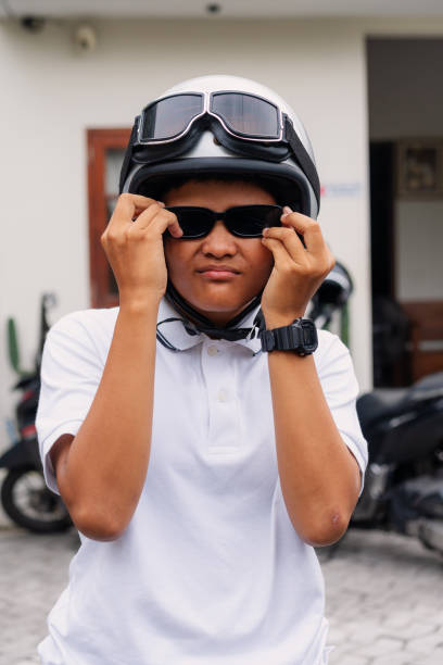 Portrait of young attractive Asian men wearing black leather jacket and sunglasses smiling while holding motorbike helmet, racer biker rider over cloudy blue sky outdoor scenery background