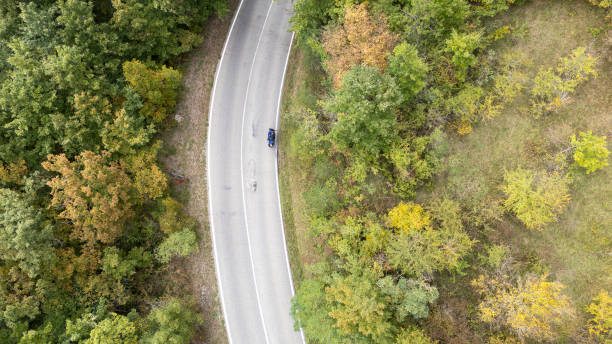 istock Man on moped scooter riding uphill on winding road through forest in autumn 2200514595