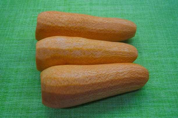Three freshly harvested orange carrots rest on a bright green textile surface. Their smooth skin and natural textures create a visually appealing contrast that highlights their organic freshness.