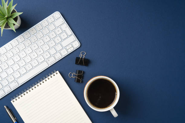 Workspace with keyboard, office supplies, pen, green leaf and coffee cup. Flat lay, top view blue office desk