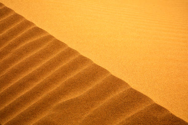 A surreal Martian-like landscape in Mongolia’s Gobi Desert, featuring rolling sand dunes and towering cliffs beneath a deep blue sky. A breathtaking view of Earth's own alien terrain.