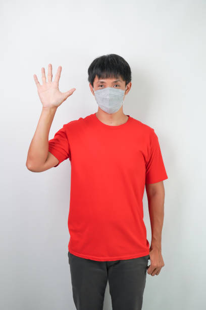 junger asiatischer mann in rot, der während der virusausbrüche eine medizinische maske trägt, hält ein smartphone mit leerem grünen bildschirm und zeigt die handgeste nummer 5, isoliert auf weißem hintergrund. - nurse high five mask stock-fotos und bilder