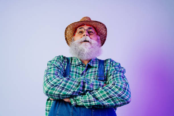 Senior old man with gray beard wearing farmer outfit portrait in studio - Funny stylish older male adult farm worker  with cool style, concepts about elderly and lifestyle