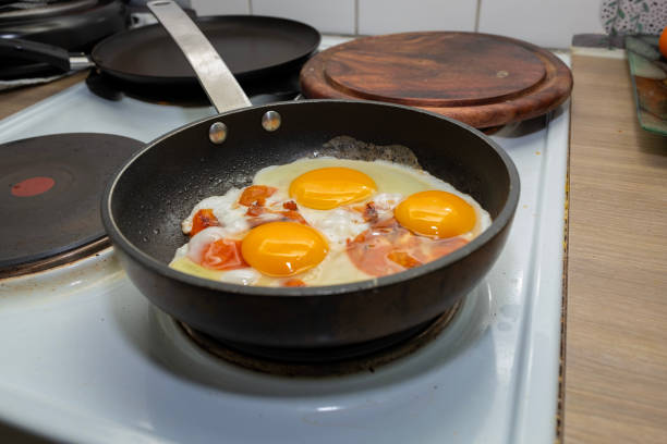 istock Fried eggs with tomatoes are cooked in a frying pan, electric stove. 2200541479