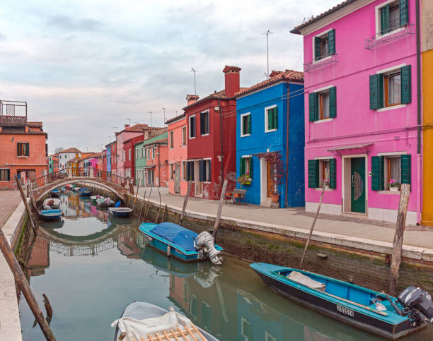 Venice, Italy - January 10, 2017: Arch Bridge Over Calm Water Canal and Colurful Houses at Burano Island Winter Afternoon.