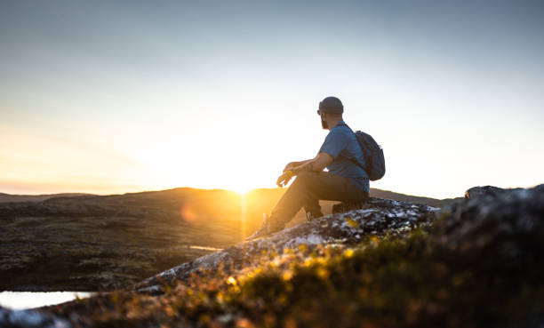 istock Adventurer sitting on a rock during a stunning sunset in the wilderness 2200542829