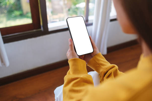 istock Mockup image of a woman holding mobile phone with blank desktop screen while sitting in bed room at home 2200543188