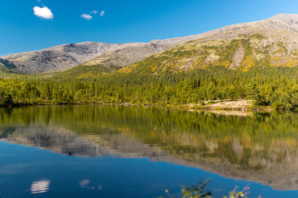 istock Serene lake reflecting trees and mountains under a vibrant blue sky 2200543862