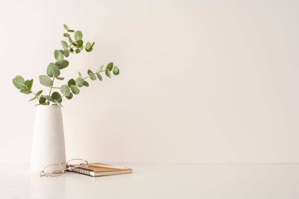 Simple and elegant minimalist setup featuring a vase with greenery, notebook, and eyeglasses