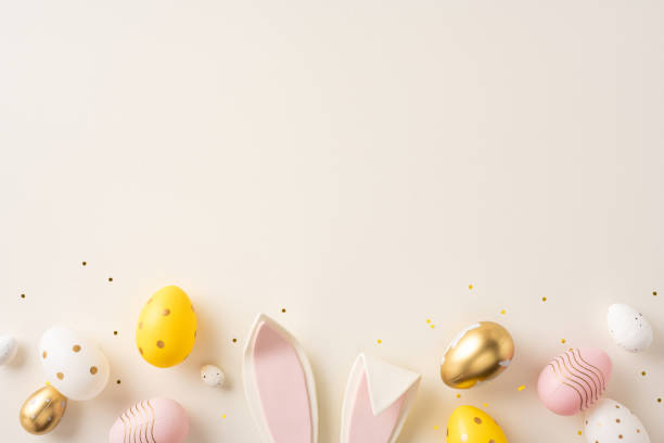 istock A variety of pastel and metallic Easter eggs with bunny ears on a soft beige background, with festive confetti, creating a warm and celebratory Easter thematic composition 2200546826