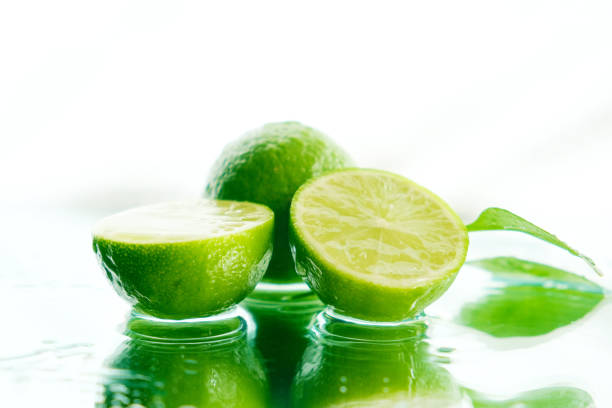 Lime fruits on mirror wet reflection surface, flowing splashing water drops. Freshness and sunlight. Tropical nature.