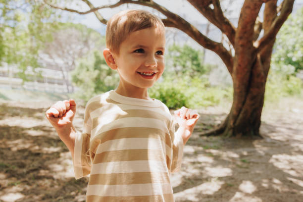 istock Cheerful young boy smiling outdoors under trees on a sunny day 2200552880