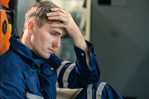 istock Man in blue work uniform appears stressed while sitting in industrial setting in the afternoon 2200561858