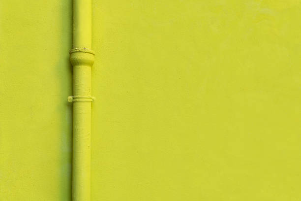 Yellow wall texture and a yellow downspout gutter of a house. Photo suitable for background or design backdrop. Copy space for graphic design.