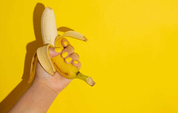 istock Female hand holding a banana on a yellow background 2200568515
