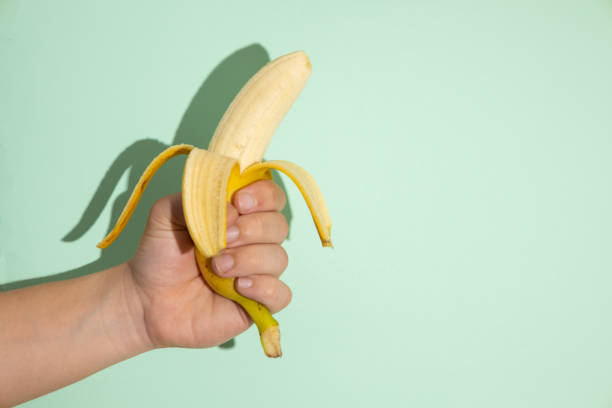 istock Male hand holding a banana on a light green background 2200568532