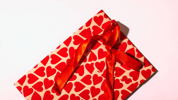 istock A beautifully wrapped Valentine's Day gift with red heart-patterned paper and a matching satin ribbon bow, placed on a white background, symbolizing love, romance, and special celebrations. 2200570056